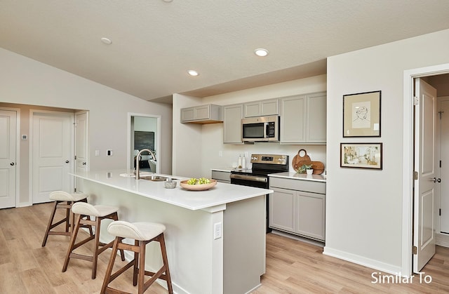 kitchen featuring a kitchen breakfast bar, stainless steel appliances, a sink, light wood-type flooring, and gray cabinetry