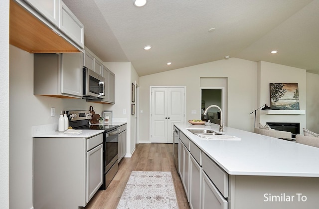 kitchen featuring lofted ceiling, stainless steel appliances, a sink, light wood-type flooring, and gray cabinets