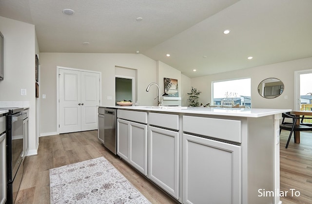 kitchen with an island with sink, light wood-style flooring, light countertops, lofted ceiling, and appliances with stainless steel finishes