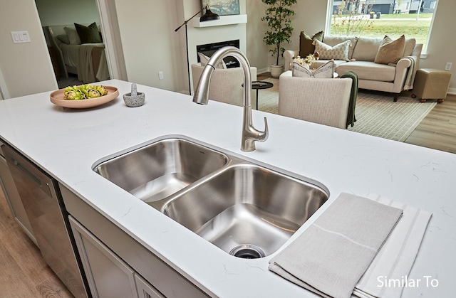 interior space featuring light wood-style flooring, a fireplace, a sink, stainless steel dishwasher, and gray cabinets