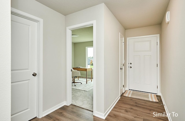 hall with a textured ceiling, dark wood-style flooring, and baseboards