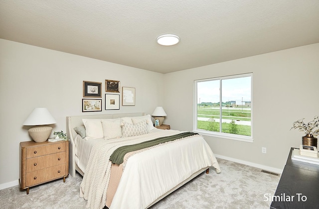 bedroom featuring a textured ceiling, light colored carpet, visible vents, and baseboards