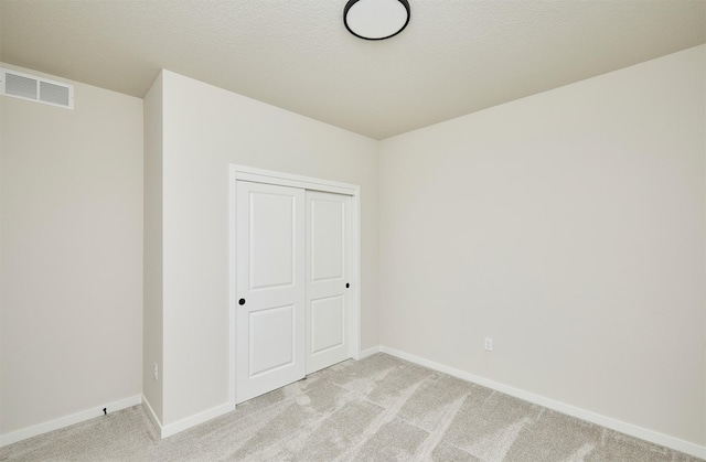 unfurnished bedroom featuring light carpet, a closet, visible vents, and baseboards