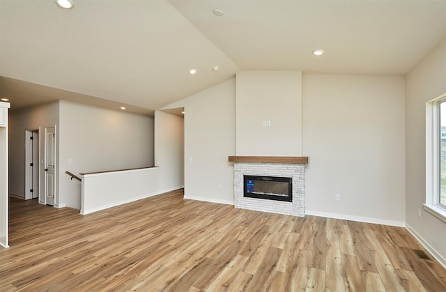 unfurnished living room featuring lofted ceiling, light wood-style flooring, a fireplace, and a healthy amount of sunlight