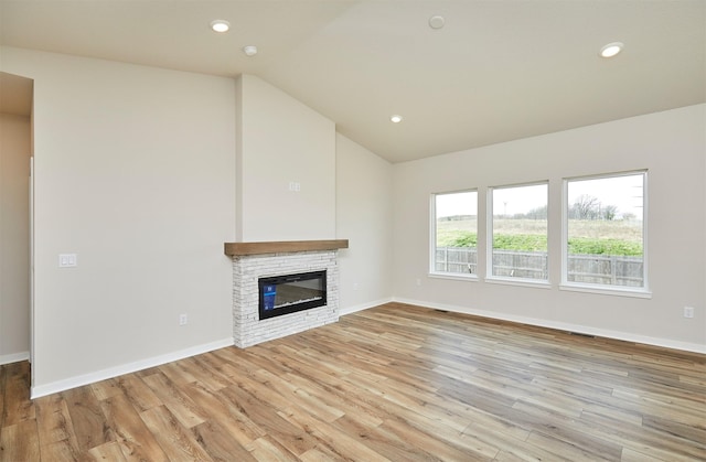 unfurnished living room featuring light wood finished floors, baseboards, vaulted ceiling, and a stone fireplace