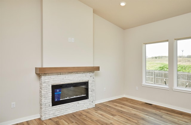 unfurnished living room featuring wood finished floors, baseboards, a stone fireplace, and visible vents