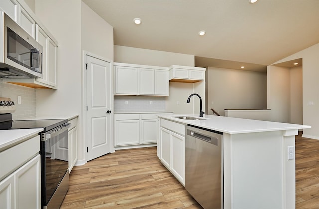 kitchen featuring tasteful backsplash, a sink, a kitchen island with sink, stainless steel appliances, and light wood-style flooring