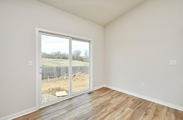 spare room featuring vaulted ceiling, visible vents, light wood finished floors, and baseboards