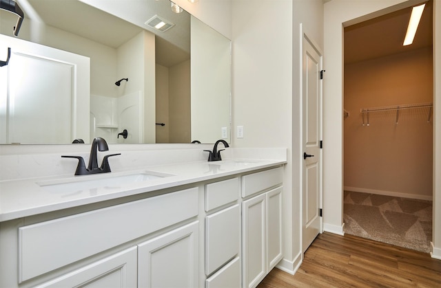 full bath with double vanity, visible vents, a sink, a walk in closet, and walk in shower