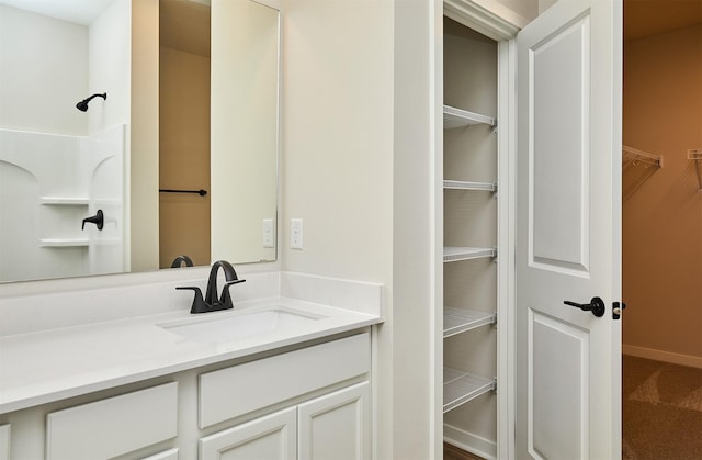bathroom featuring a walk in closet, baseboards, and vanity