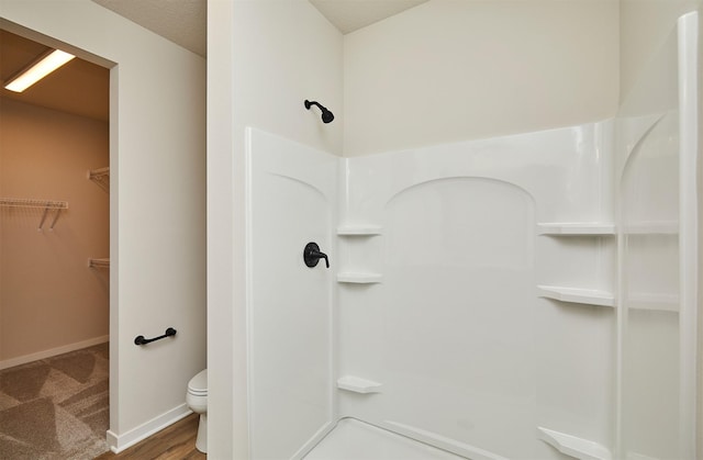 full bathroom featuring a spacious closet, toilet, baseboards, and a walk in shower