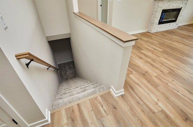 stairway featuring baseboards, a stone fireplace, and wood finished floors
