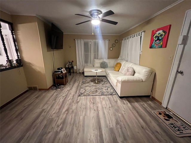 living area featuring wood finished floors, a ceiling fan, visible vents, baseboards, and ornamental molding