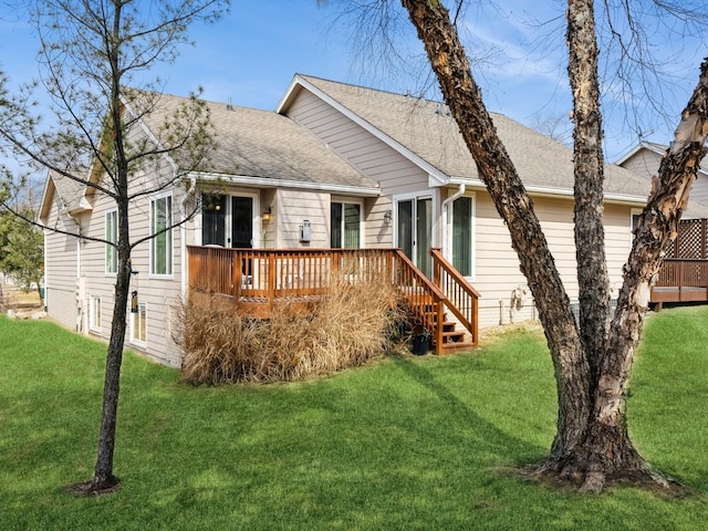 view of front of home with a deck, roof with shingles, and a front yard