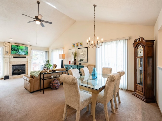 dining space with light carpet, high vaulted ceiling, ceiling fan with notable chandelier, and a glass covered fireplace