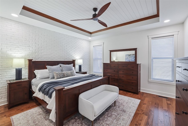 bedroom featuring brick wall, a raised ceiling, and dark wood-style flooring