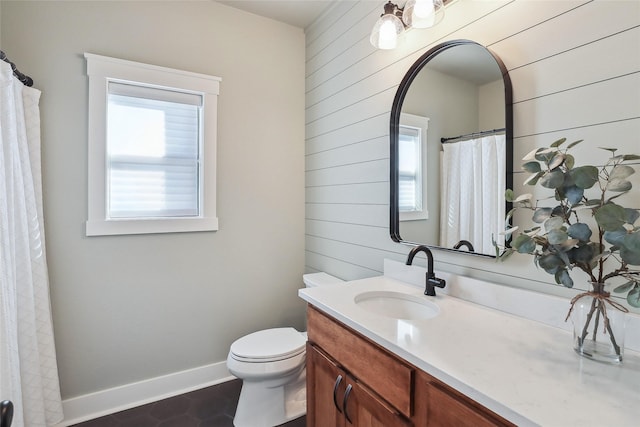 bathroom featuring toilet, wooden walls, baseboards, and vanity