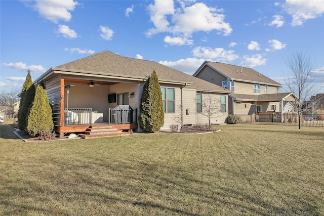 rear view of house featuring ceiling fan, a deck, a shingled roof, fence, and a yard