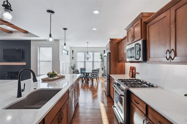 kitchen with a sink, hanging light fixtures, appliances with stainless steel finishes, light countertops, and brown cabinetry