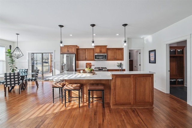 kitchen featuring light countertops, appliances with stainless steel finishes, a large island, brown cabinetry, and wood-type flooring