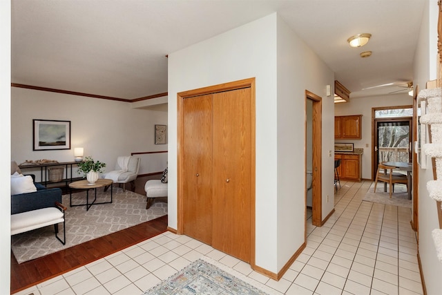 hallway featuring light tile patterned floors, ornamental molding, and baseboards