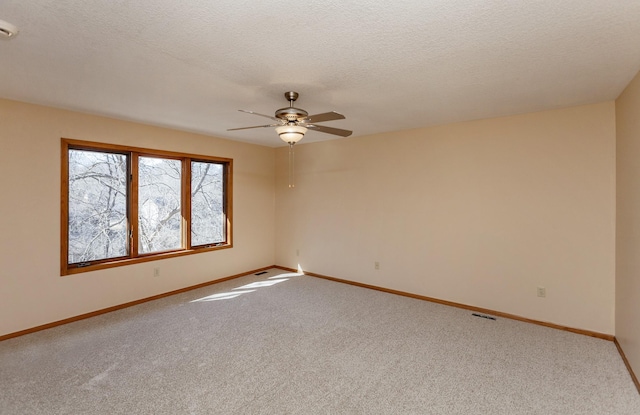 carpeted spare room with a ceiling fan, visible vents, a textured ceiling, and baseboards