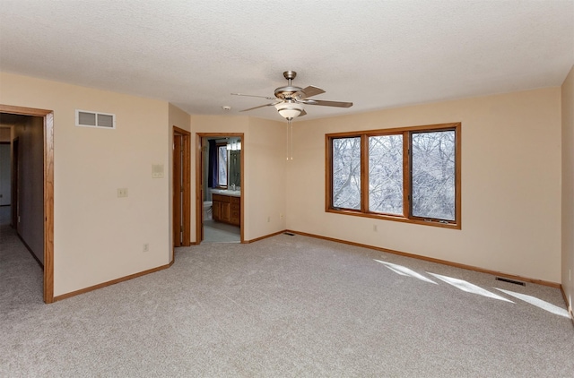 empty room with light carpet, visible vents, a textured ceiling, and baseboards