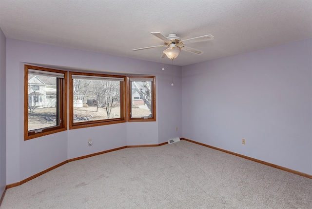 carpeted spare room featuring visible vents, ceiling fan, a textured ceiling, and baseboards