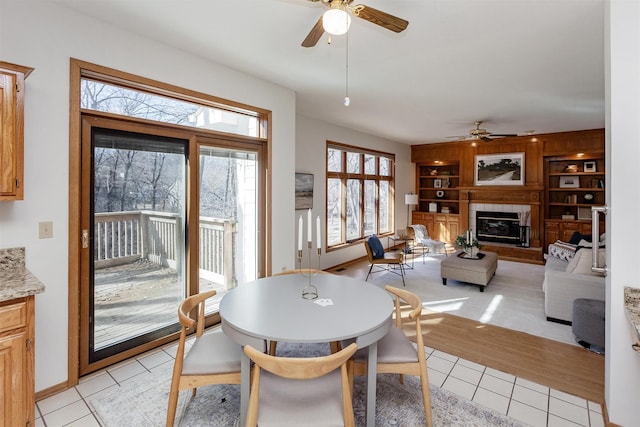 dining area with light tile patterned floors, built in features, baseboards, a tile fireplace, and ceiling fan