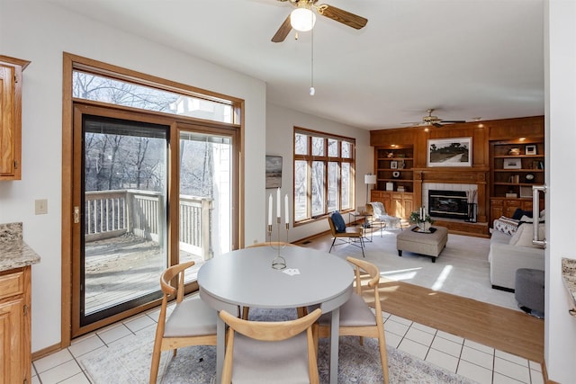 dining area featuring baseboards, built in shelves, a ceiling fan, a fireplace, and light tile patterned floors