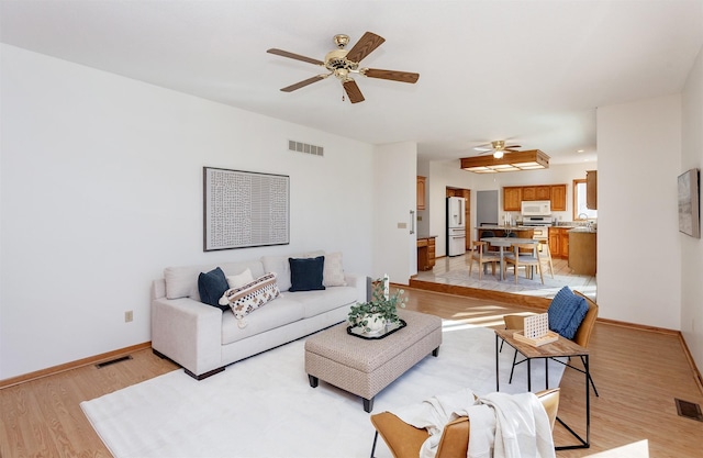 living area featuring light wood-style flooring, a ceiling fan, visible vents, and baseboards