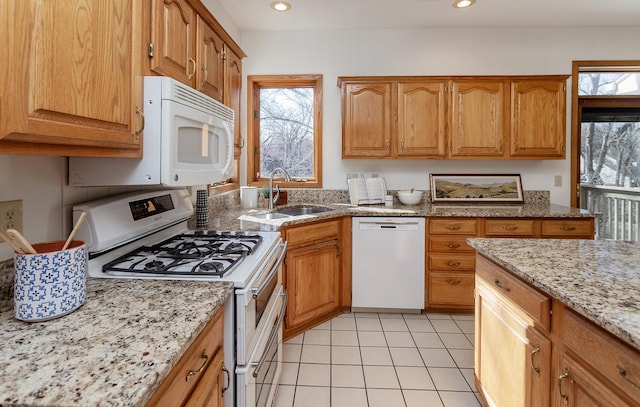 kitchen with a sink, brown cabinetry, light tile patterned flooring, white appliances, and light stone countertops