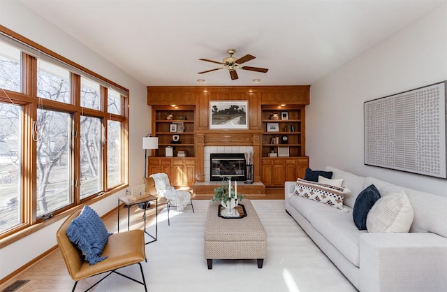 living area featuring baseboards, visible vents, built in features, ceiling fan, and a fireplace