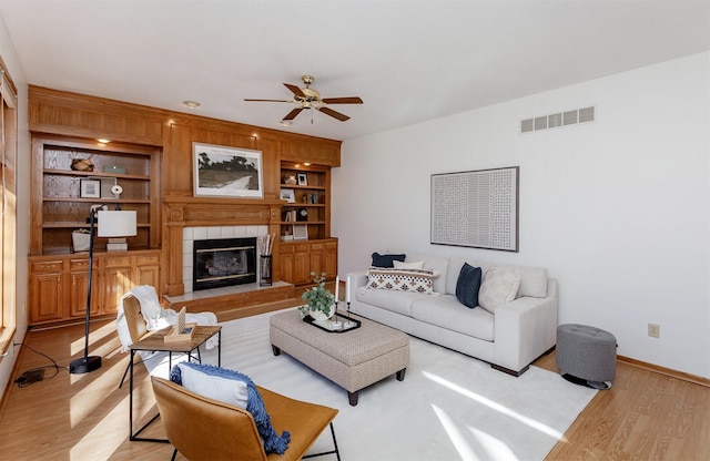 living room with light wood-type flooring, visible vents, a ceiling fan, and built in shelves