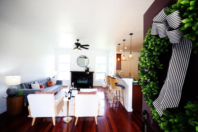 living area with a ceiling fan, a fireplace, and dark wood finished floors