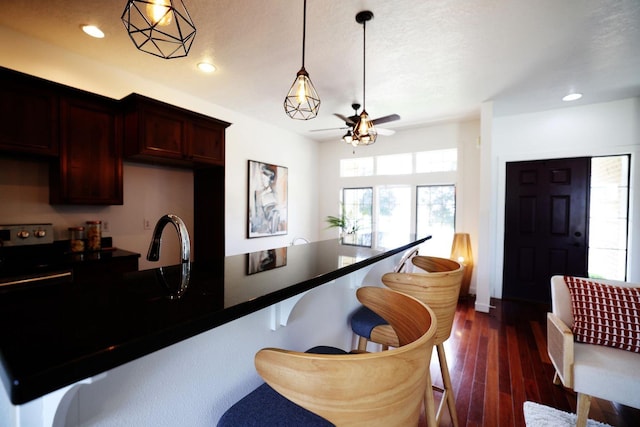 kitchen with decorative light fixtures, dark wood finished floors, dark countertops, recessed lighting, and a kitchen bar