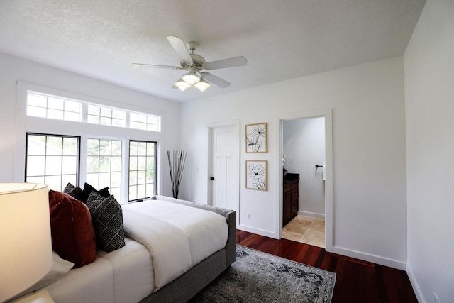 bedroom with a textured ceiling, wood finished floors, a ceiling fan, baseboards, and ensuite bath