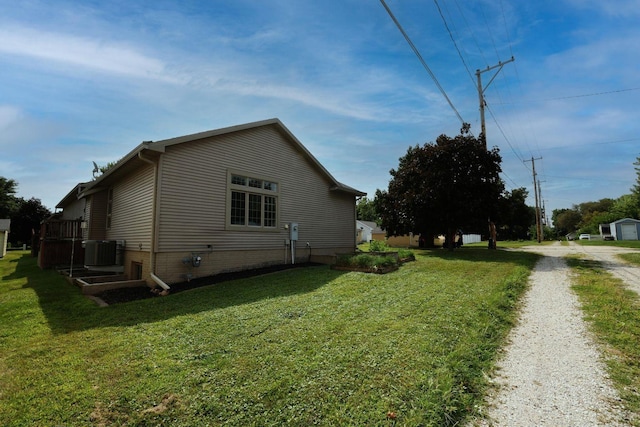 view of side of property featuring driveway, central air condition unit, and a yard