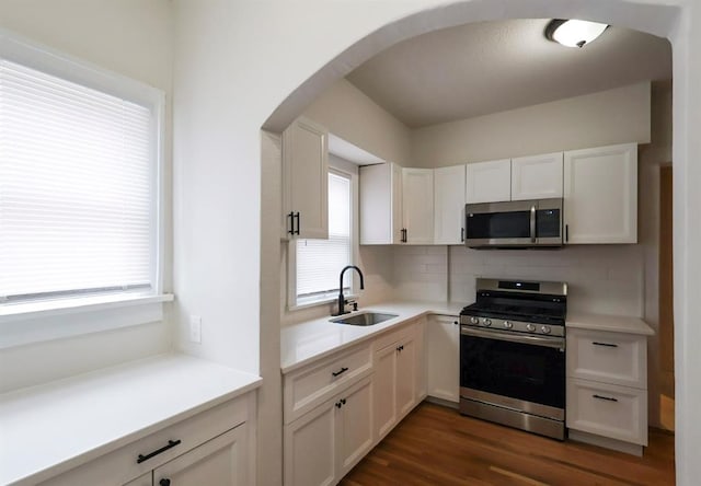 kitchen featuring dark wood-style flooring, a sink, white cabinets, appliances with stainless steel finishes, and decorative backsplash