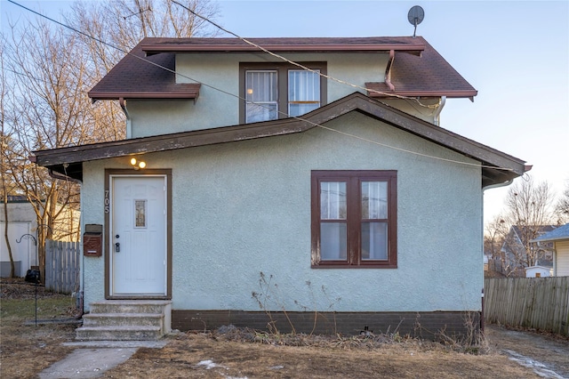 view of front facade with entry steps, roof with shingles, fence, and stucco siding