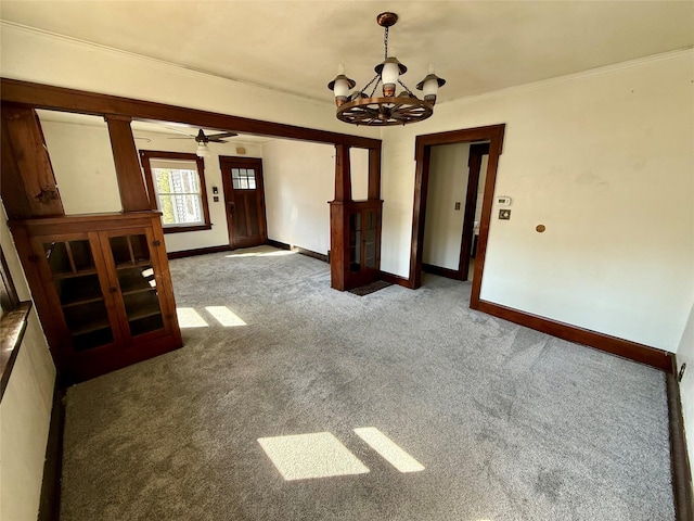 carpeted empty room featuring an inviting chandelier, crown molding, and baseboards