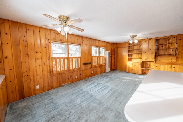 unfurnished living room featuring visible vents, a ceiling fan, light carpet, wood walls, and a textured ceiling