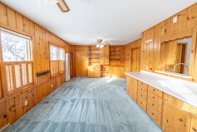 interior space featuring wooden walls, visible vents, built in features, light colored carpet, and ceiling fan