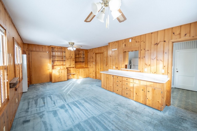 interior space featuring light carpet, wooden walls, light countertops, and a ceiling fan