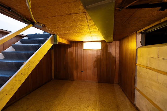 basement with stairs, light floors, and wood walls