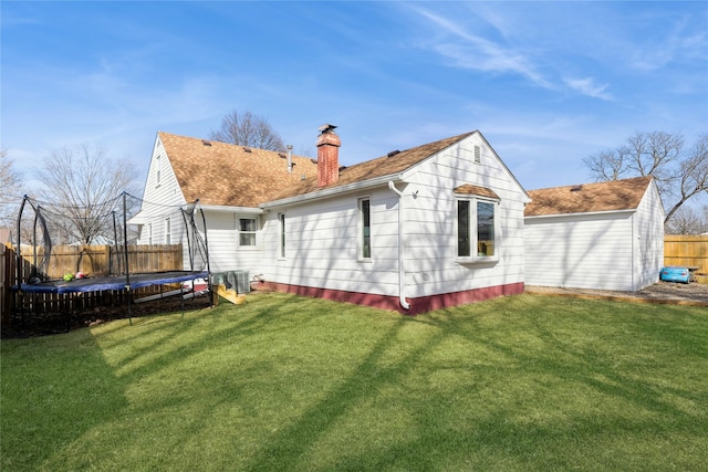 rear view of house with a chimney, a trampoline, fence, and a lawn