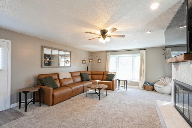 living room featuring ceiling fan, a textured ceiling, a fireplace with flush hearth, baseboards, and carpet