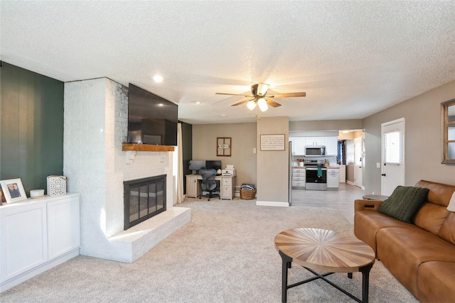 living room with a textured ceiling, ceiling fan, a fireplace, and light colored carpet