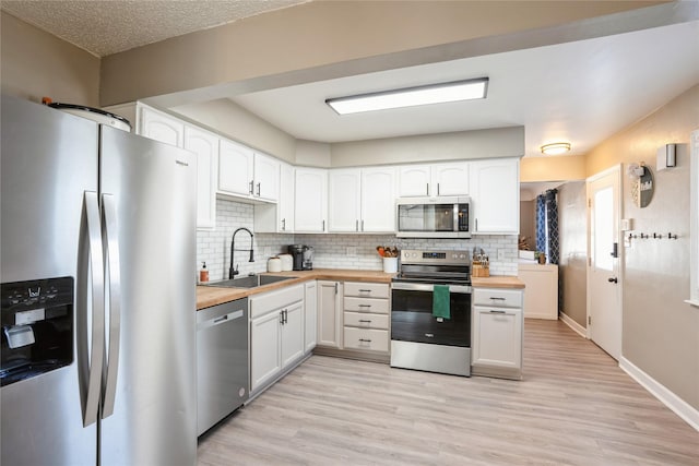 kitchen with white cabinets, decorative backsplash, wood counters, stainless steel appliances, and a sink