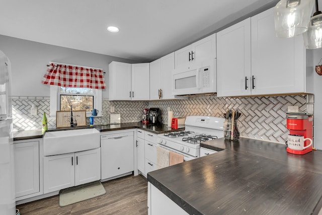 kitchen with dark countertops, white appliances, white cabinetry, and a sink